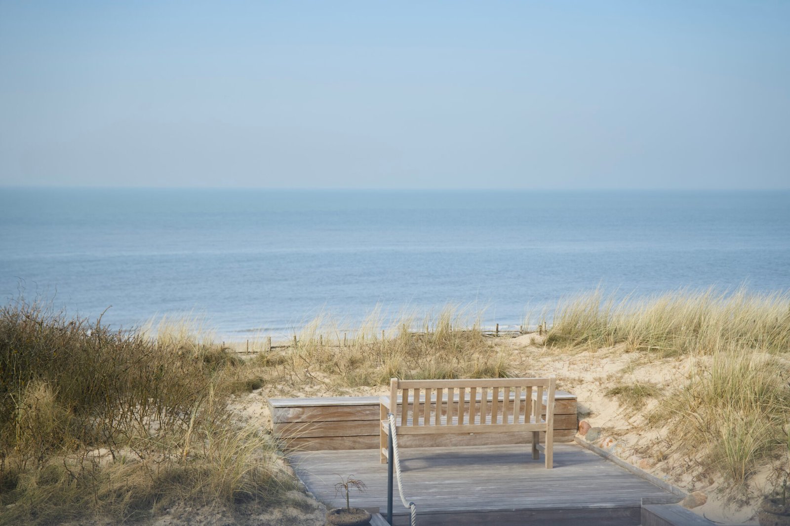 Eine Bank auf der Terrasse, Dünen, das Meer – der Urlaubsblick vom Söl’ring Hof Sylt.