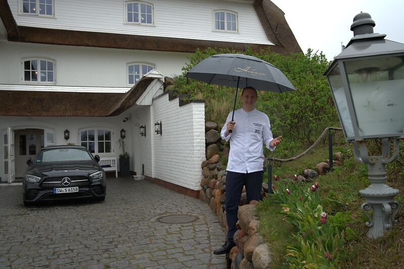 Mann mit Regenschirm am Söl’ring Hof auf Sylt, blühende Tulpen.