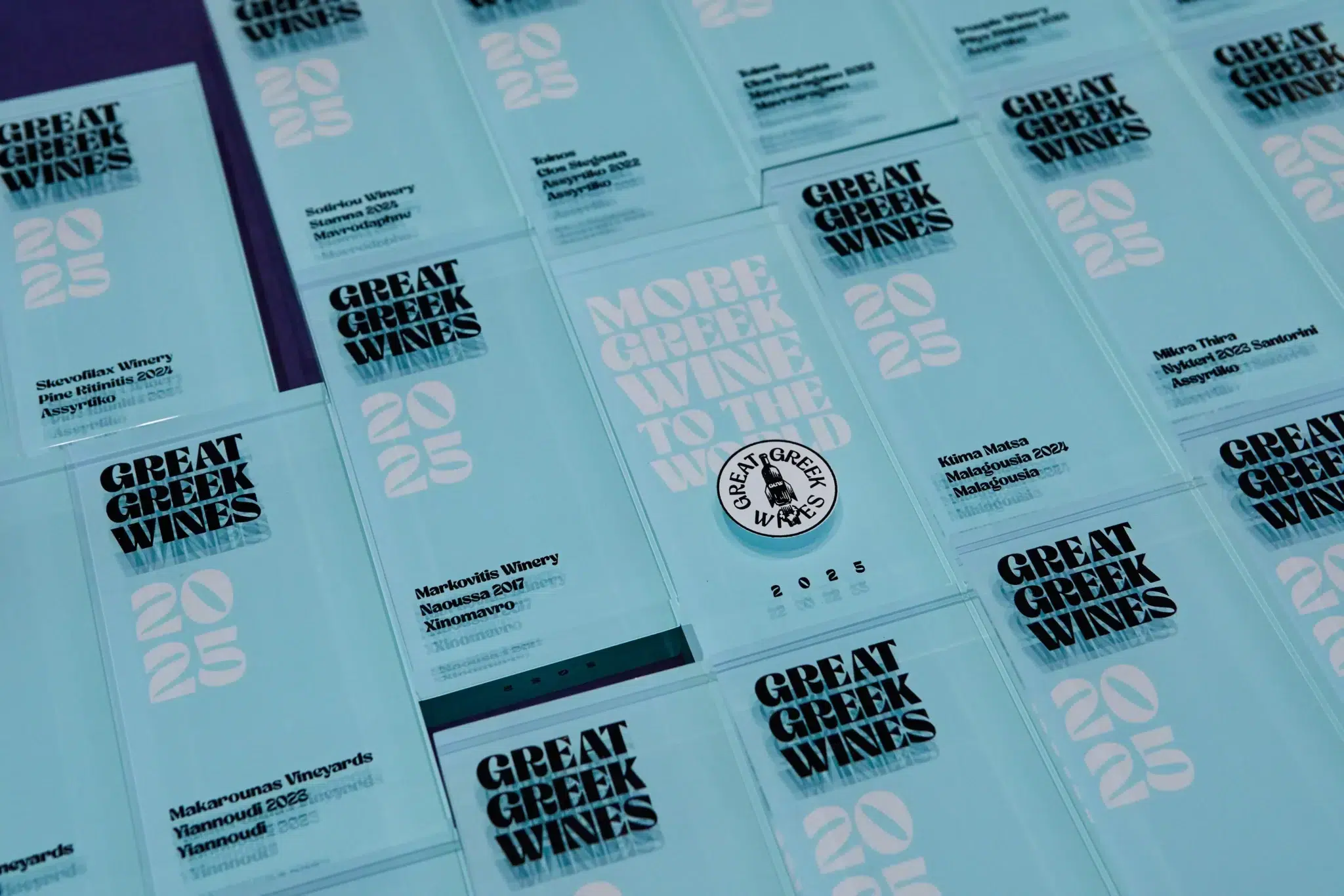 Auf den durchsichtigen blauen Schildern steht "GREAT GREEK WINES 2025" mit Details.