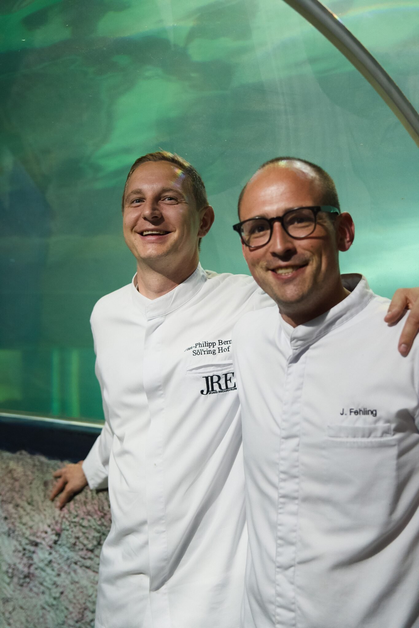 Zwei Köche lächeln im Aquarientunnel bei der Weinveranstaltung des Söl'ring Hofs.