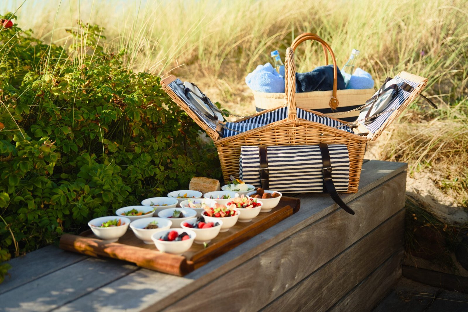 Offener Picknickkorb auf der Bank mit Snacks, Obst und Handtüchern.
