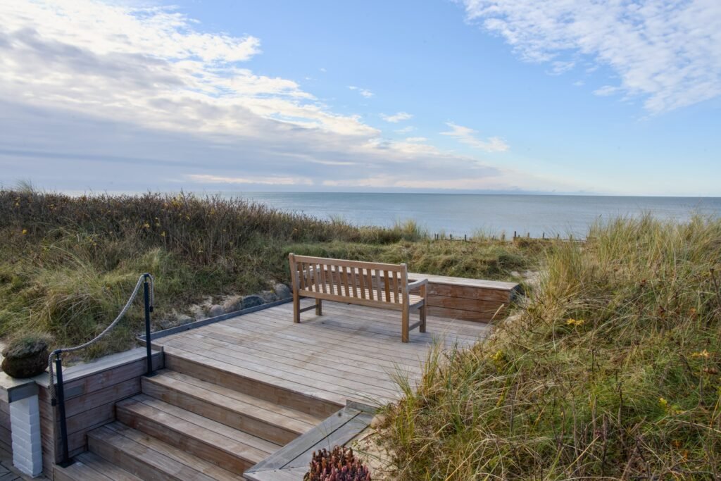 Holzbank auf Deck über den Dünen, Blick aufs Meer, bewölkter Himmel.