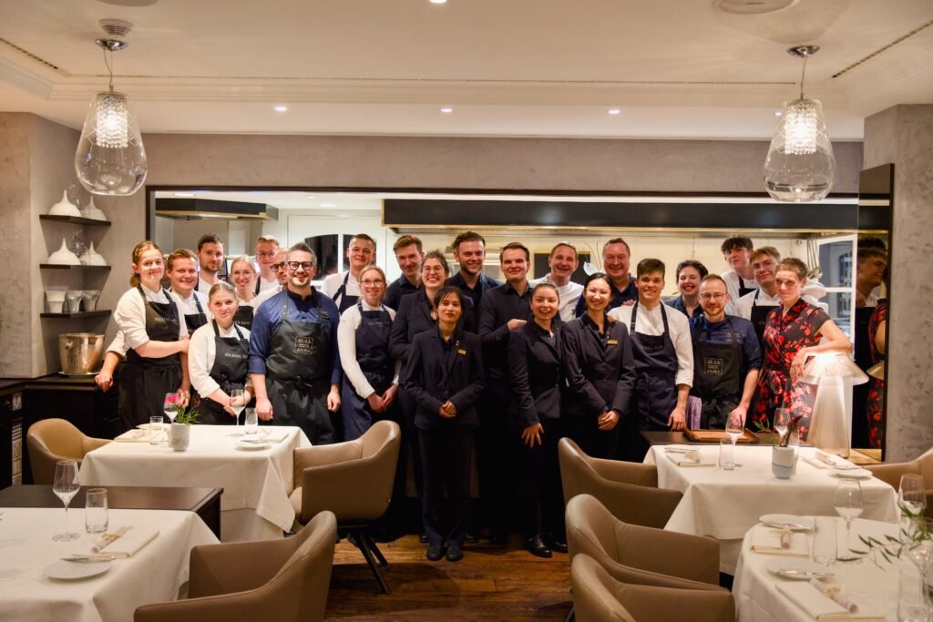 Restaurantmitarbeiter und Köche posieren gemeinsam in einem hellen Speisesaal.