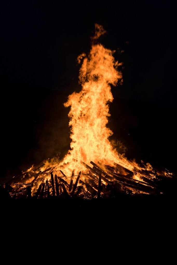 Ein Lagerfeuer mit hohen Flammen brennt hell in der Dunkelheit; die Umgebung ist schattig.