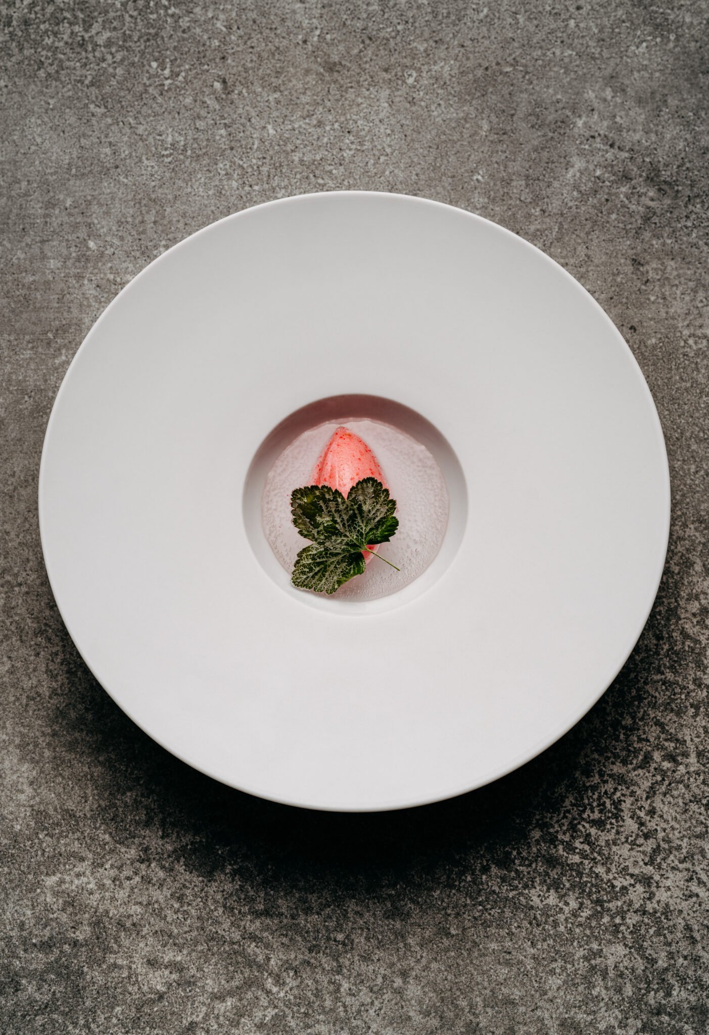 Rosa Sorbet mit Minze auf einem weißen Teller, grauer Hintergrund.