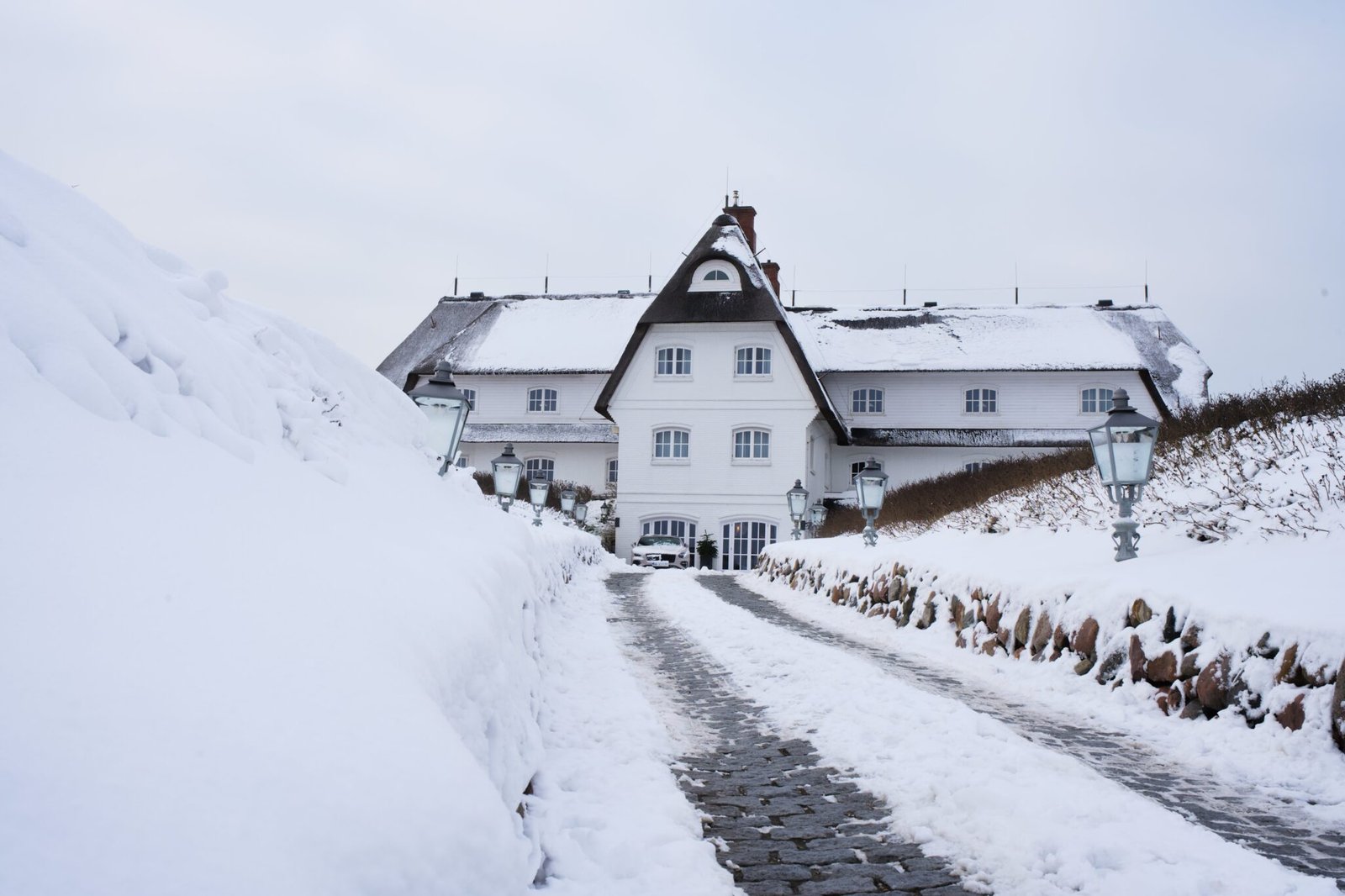 White house with steep roof at snowy path, cloudy sky.