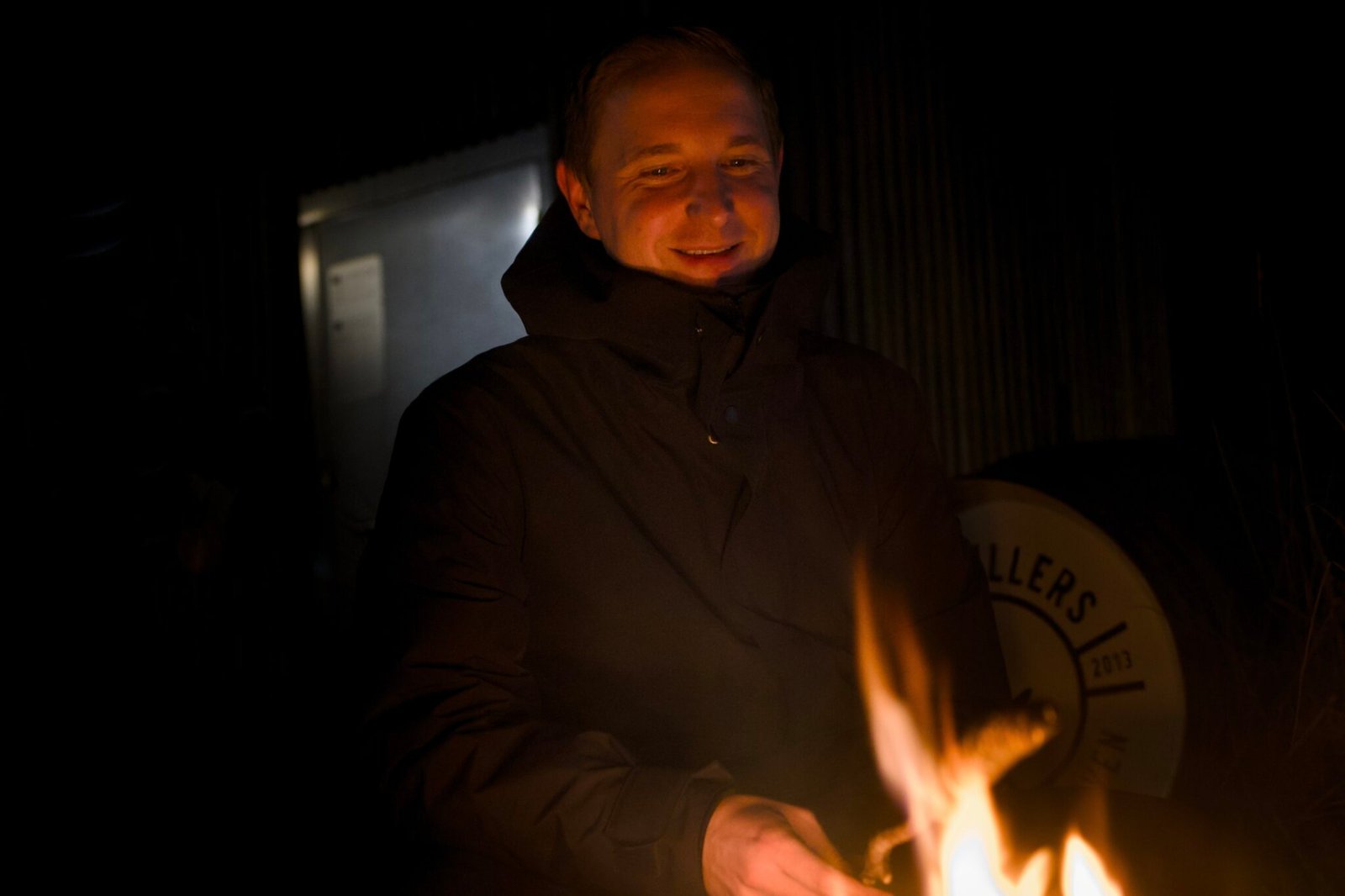 Person in dark jacket by night fire, dim metal background.