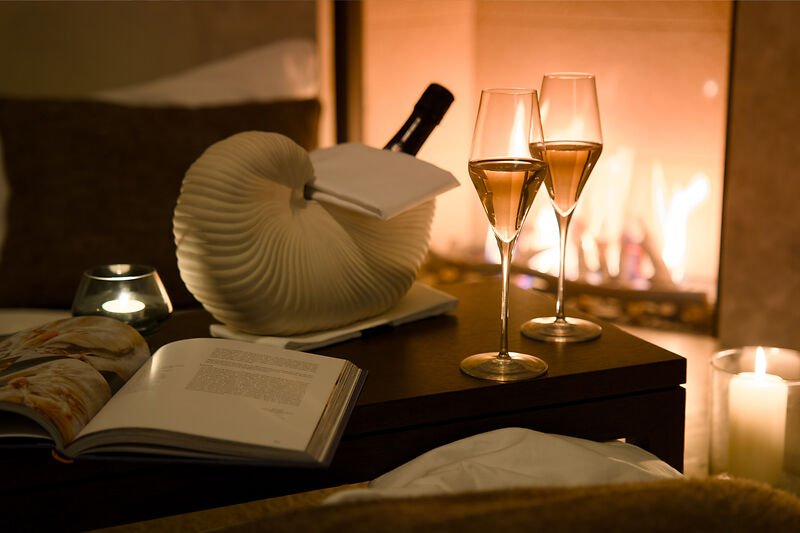 Champagnergläser, Buch, Wein und Kerze auf dem Tisch am Kamin.