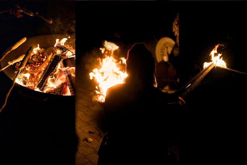 Menschen rösten Essen auf Stöcken an einem nächtlichen Feuer, im Schattenriss.