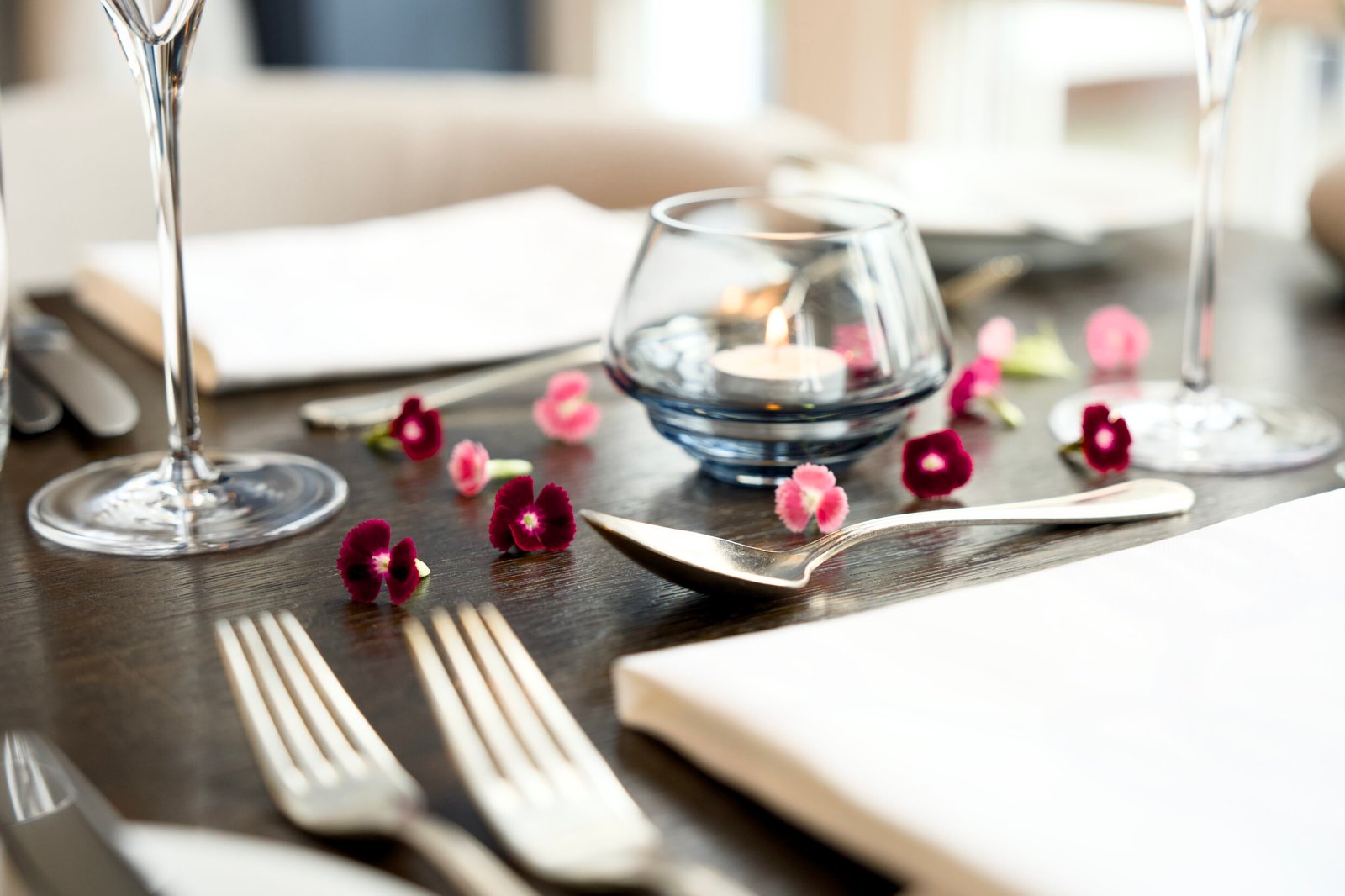Romantischer Restauranttisch mit Besteck, Servietten, Blütenblättern und Kerzenständer.