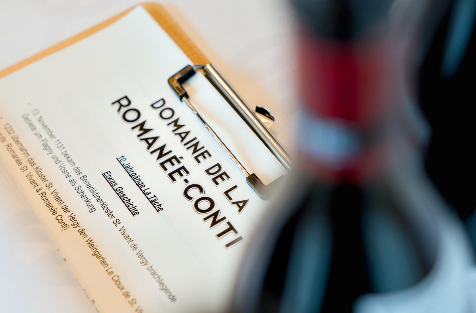 Klemmbrett mit "Domaine de la Romanée-Conti" Papier, Flasche verwischt Text.