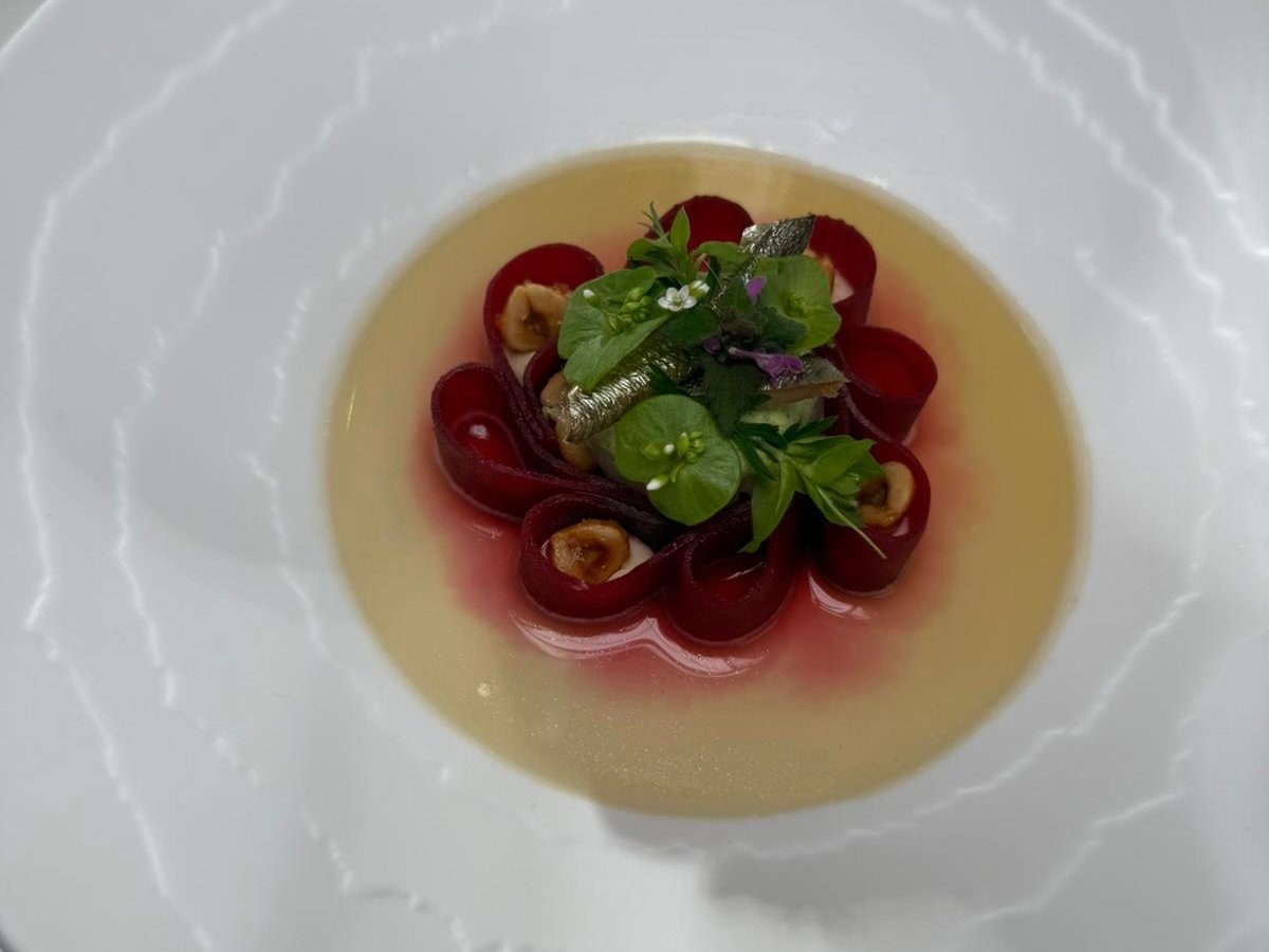 Klare Brühe mit rotem Gemüse, Kräutern, Blumen, Nüssen, Fisch.