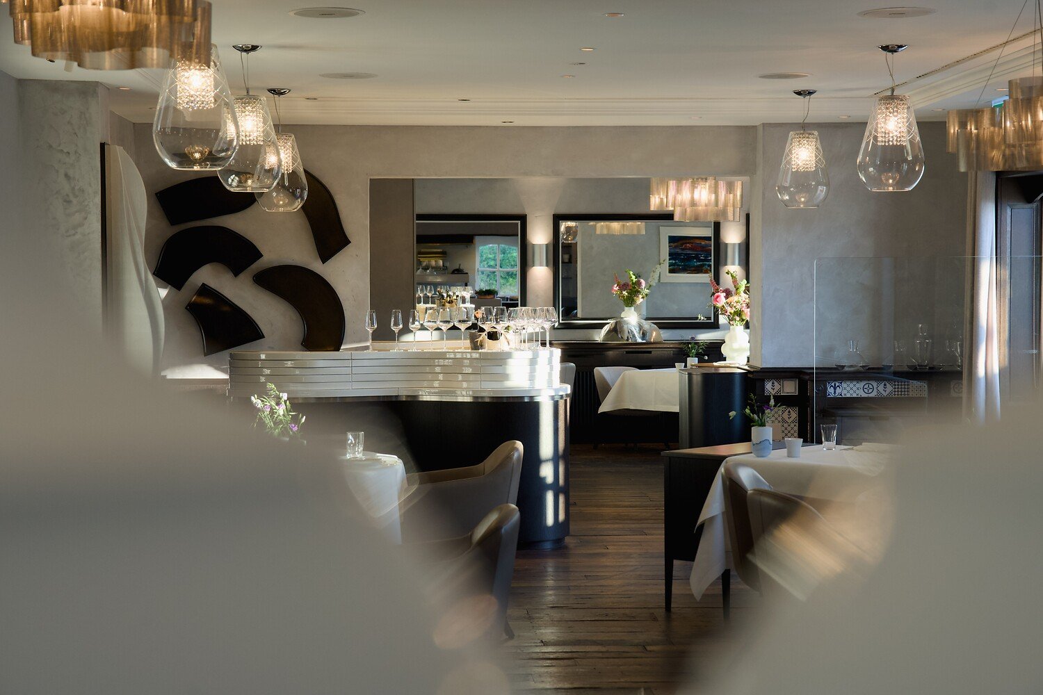 Modernes Restaurant, Hängelampen, weiße Tischdecken, Weingläser, sanfte Beleuchtung.