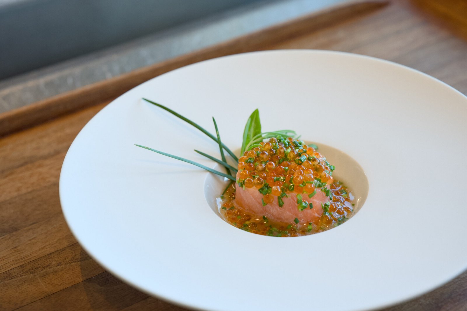 Raw fish with roe, herbs, chives on white plate.
