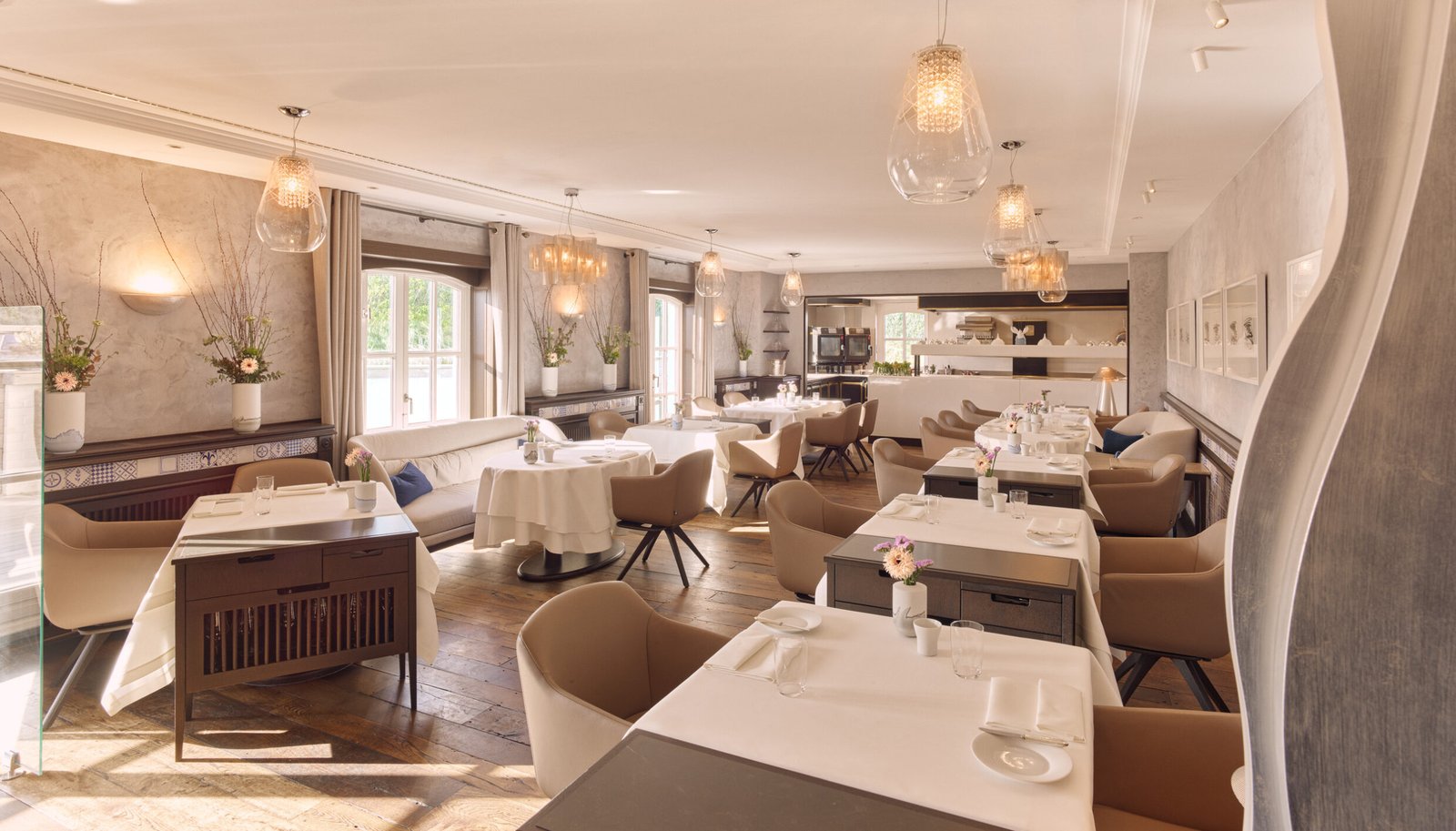Modern dining room: white tablecloths, beige chairs, wood floor, flowers.