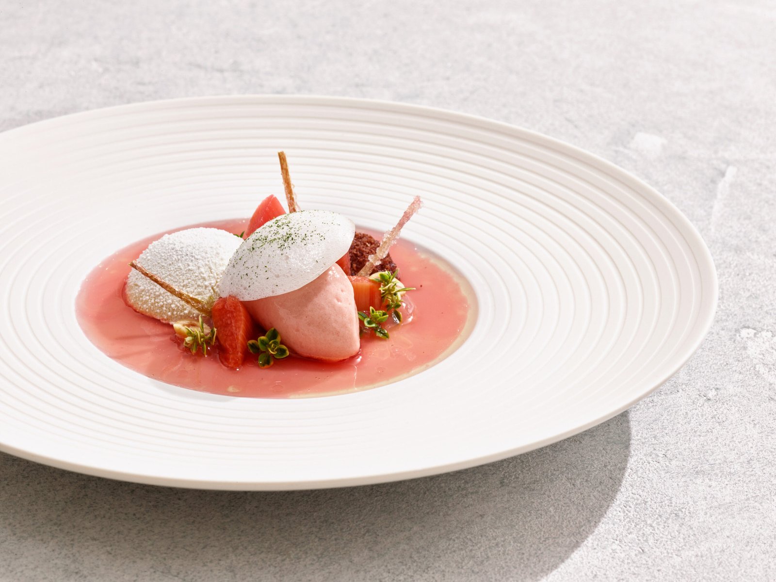 Künstlerisch angerichteter Teller: rosa Sorbet, Biskuit, Streusel, Obst, Garnitur.