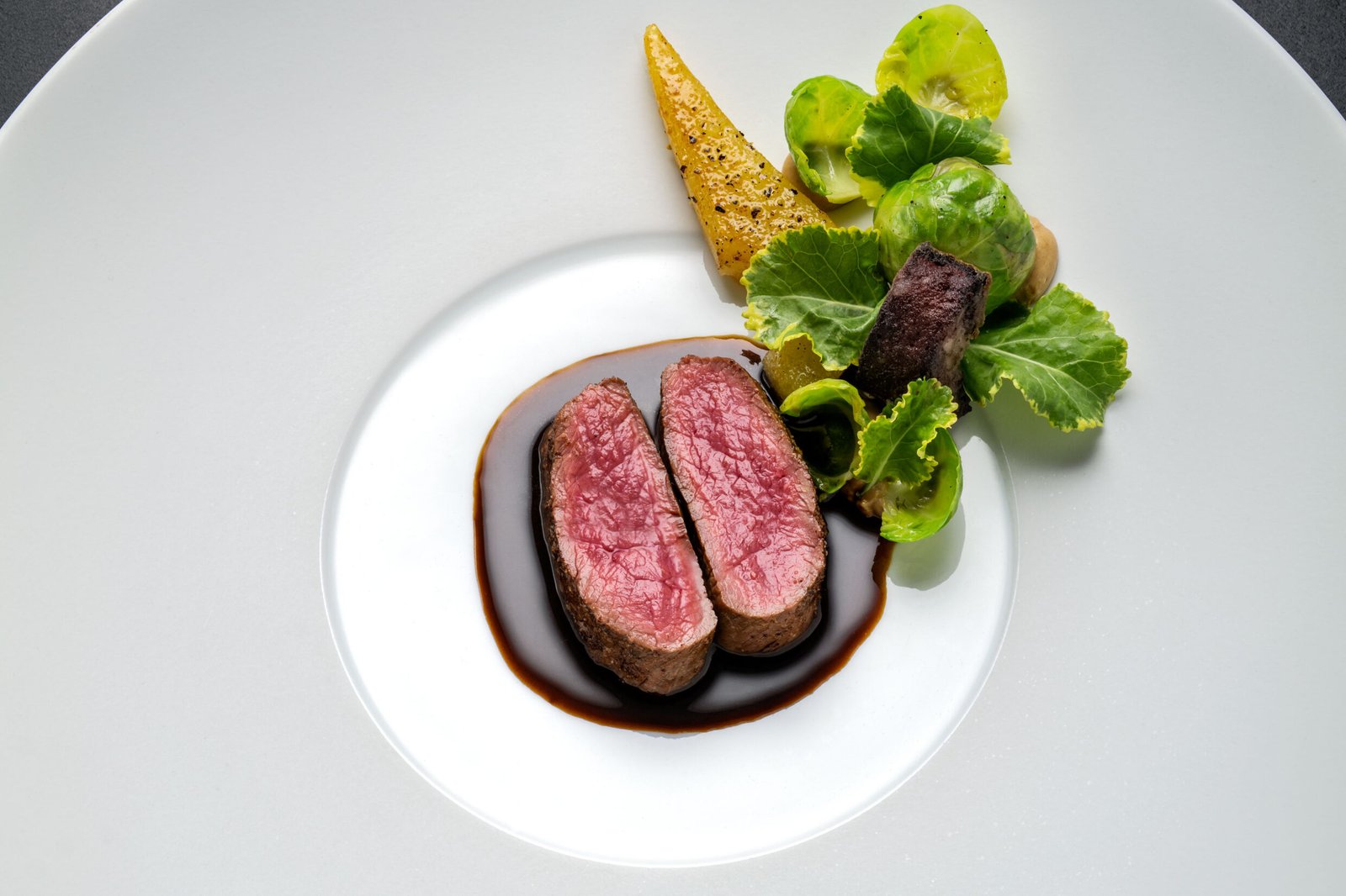 Medium-rare gebratenes Fleisch, dunkle Soße, Möhren und Rosenkohl auf einem weißen Teller.