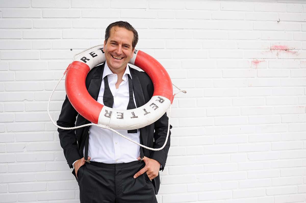 Smiling man in suit with red lifebuoy around neck.