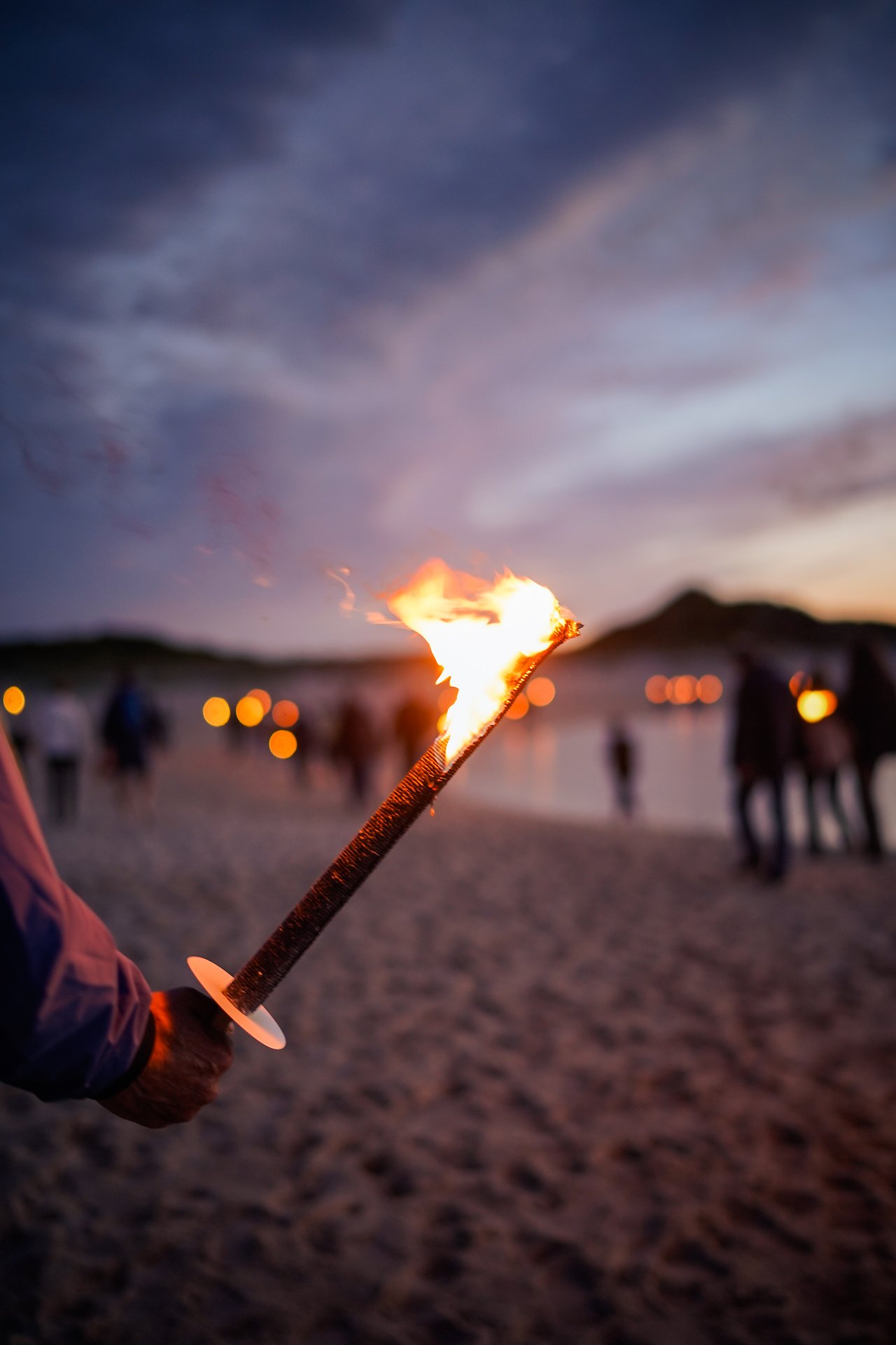 Hand hält brennende Fackel am Strand bei Dämmerung