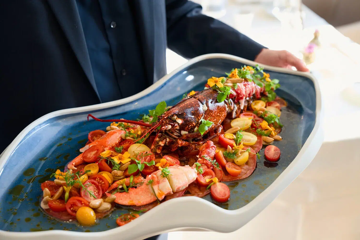 Blaue Platte mit einem ganzen Hummer, Tomaten, Bohnen, Microgreens und Blütenblättern.