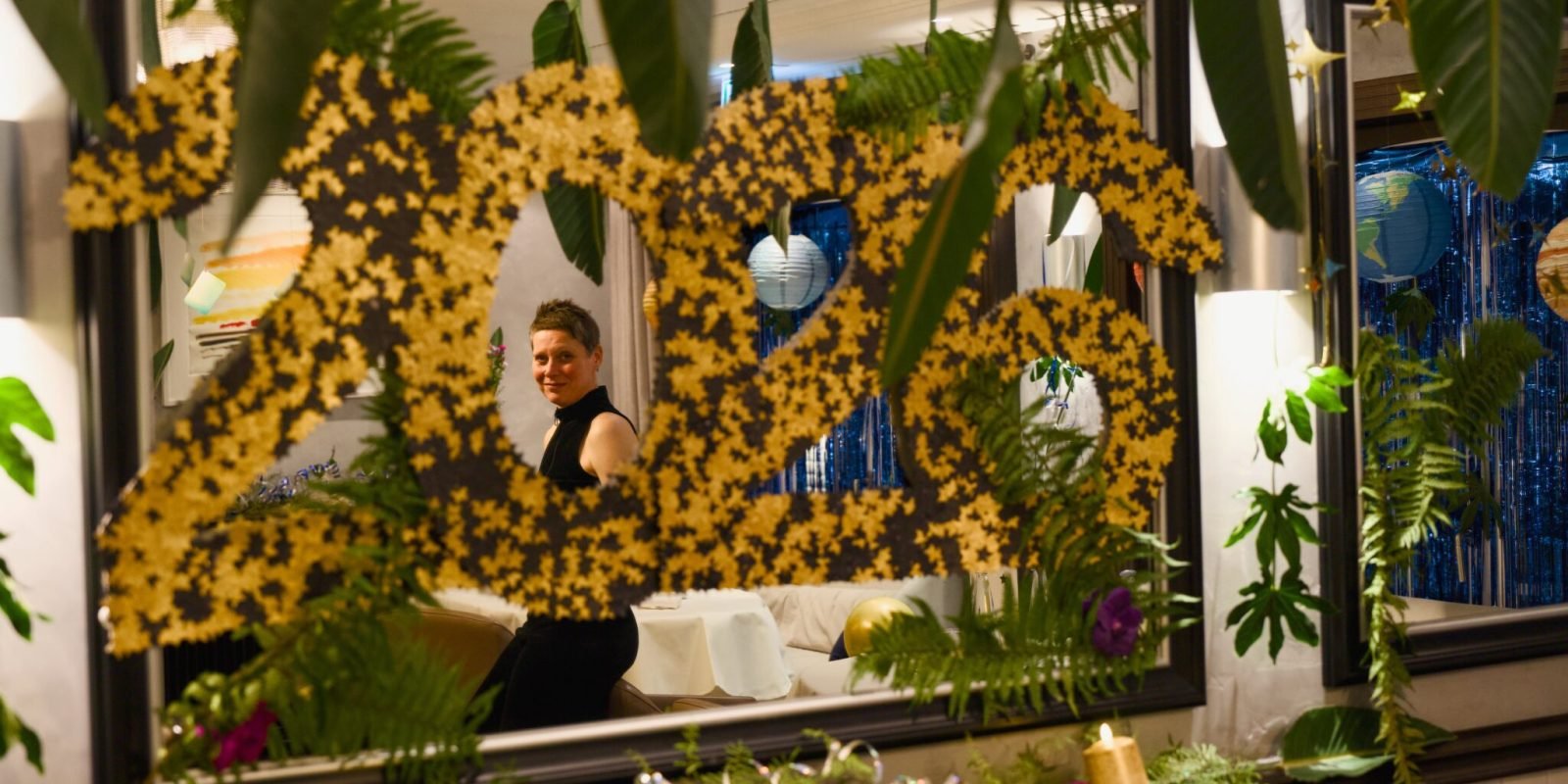 Mirror with yellow flower "2024," reflection, plants, candles, decorations.