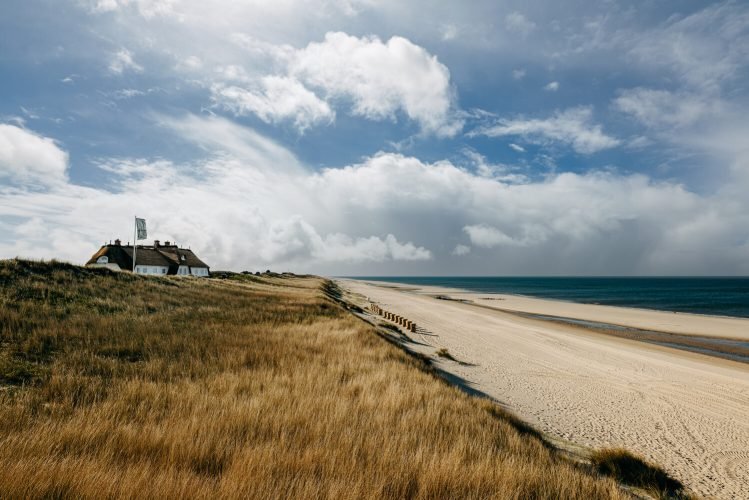 Söl’ring Hof Sylt: weißes Haus, Leuchtturm, Strand, Gras, Meer.