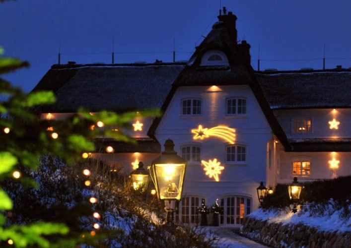 Reetdachhaus mit Sternenlichtern, verschneitem Weg und beleuchtetem Baum.
